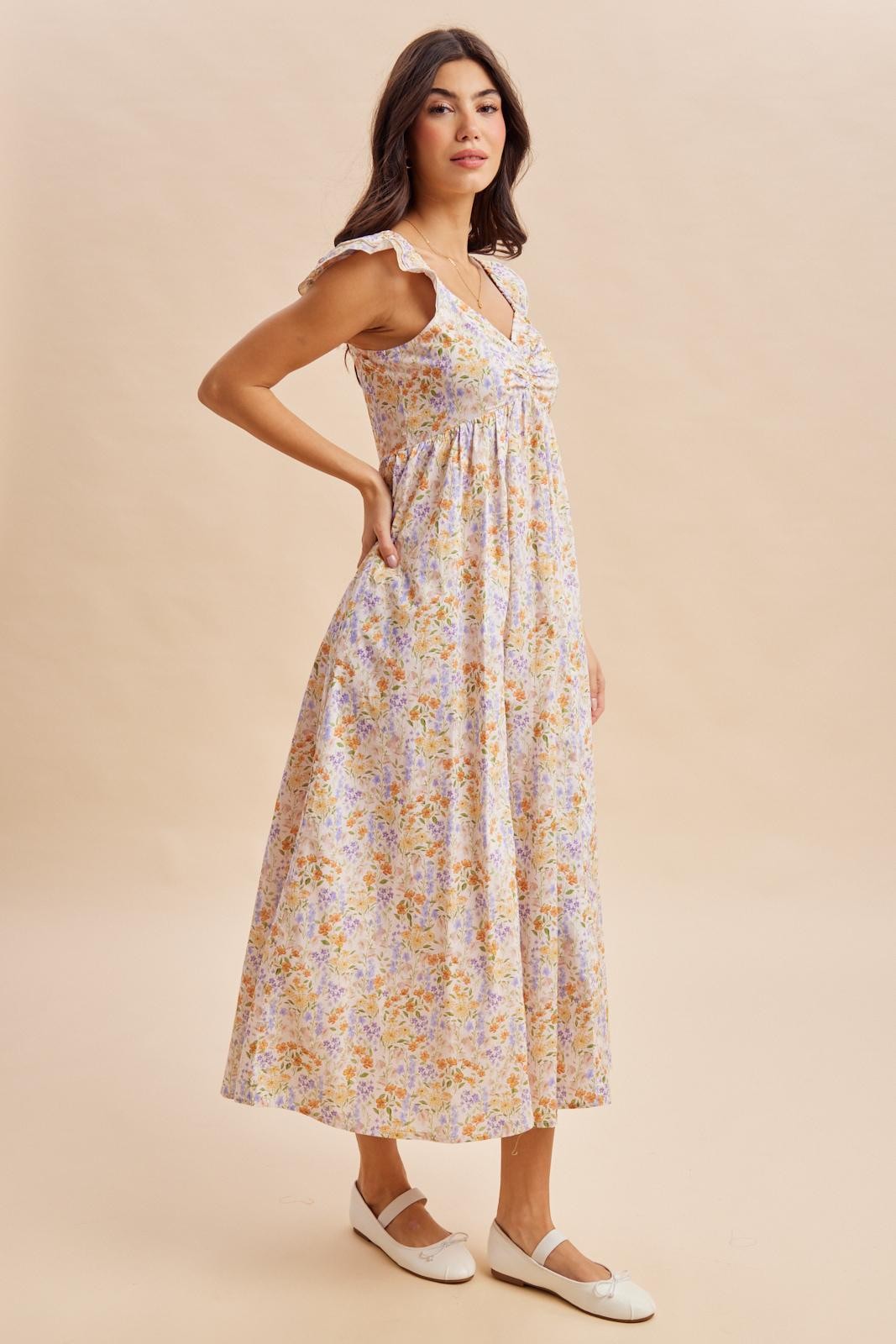 woman wearing a floral maxi dress with ruffle straps and a cinched waist, standing in profile on a neutral background