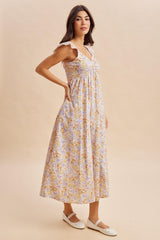 woman wearing a floral maxi dress with ruffle straps and a cinched waist, standing in profile on a neutral background