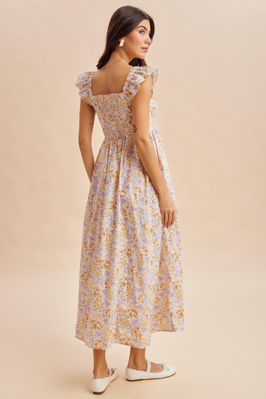 woman wearing a floral maxi dress with ruffled sleeves and a fitted bodice, standing with her back to the camera