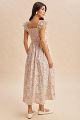 woman wearing a floral maxi dress with ruffled sleeves and a fitted bodice, standing with her back to the camera