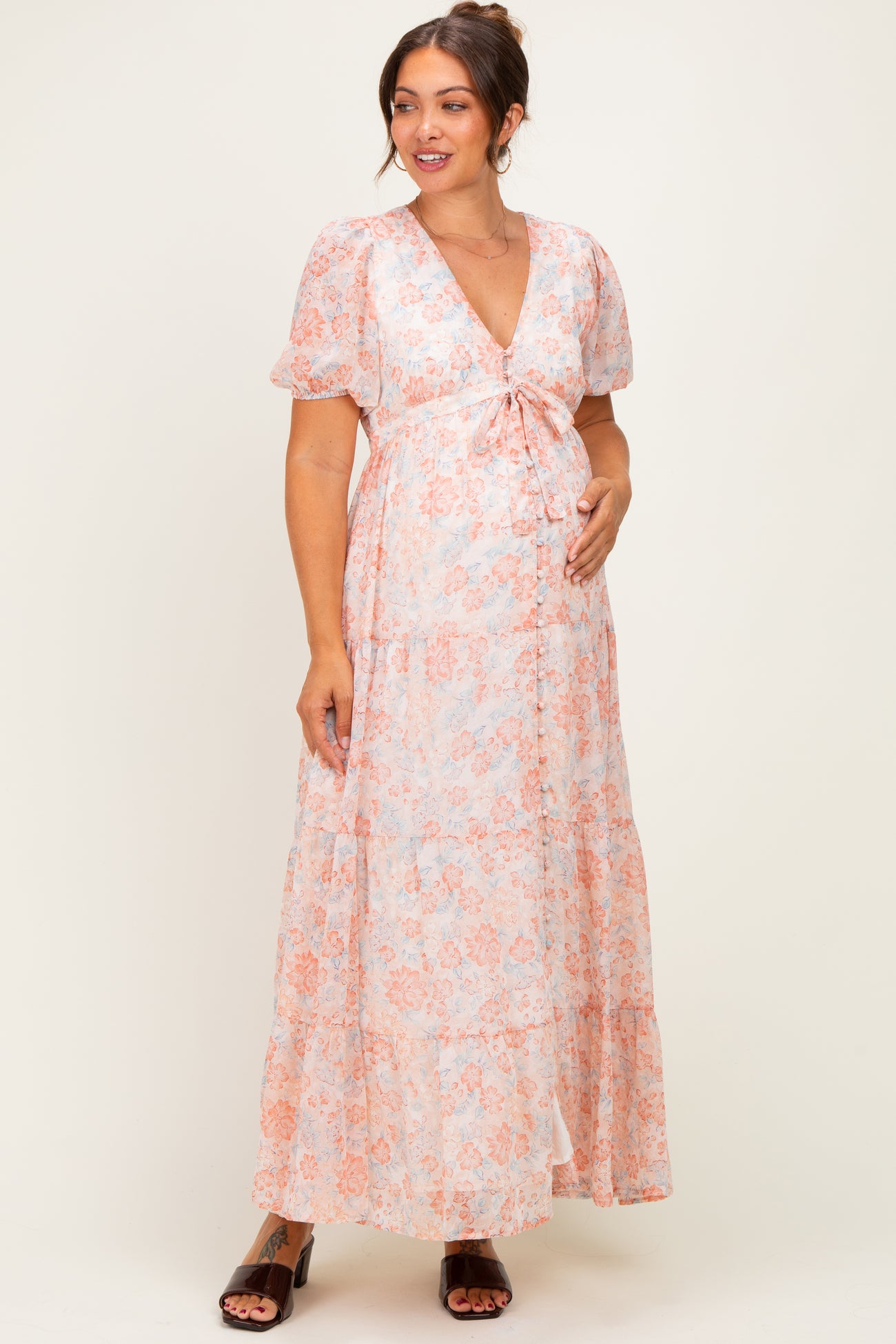 woman wearing a floral light pink maternity maxi dress with short sleeves and a tie front, holding her baby bump