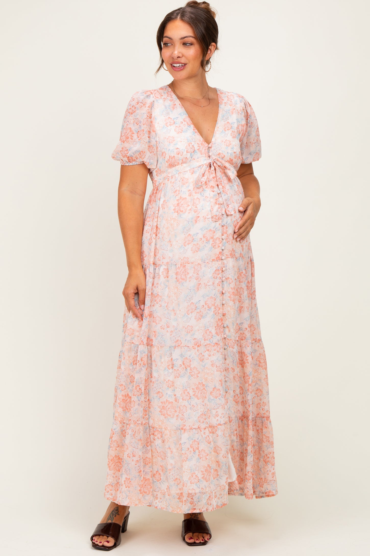 woman wearing a floral light pink maternity maxi dress with short sleeves and a tie front, holding her baby bump