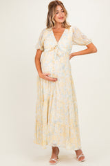 woman wearing a yellow floral maternity maxi dress with a tie front and puff sleeves, showing her baby bump