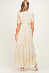 woman wearing a flowy yellow floral maternity dress, view of the back with short puff sleeves and gathered waist