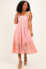 woman wearing a pink lace mid-length dress with smocked bodice and ribbon straps, posing with a smile