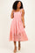woman wearing a pink lace mid-length dress with smocked bodice and ribbon straps, posing with a smile