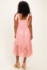 woman wearing a pink lace midi dress with smocked bodice and tie straps, standing with her back to the camera