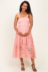 woman wearing a pink lace maternity dress with spaghetti straps and a visible baby bump
