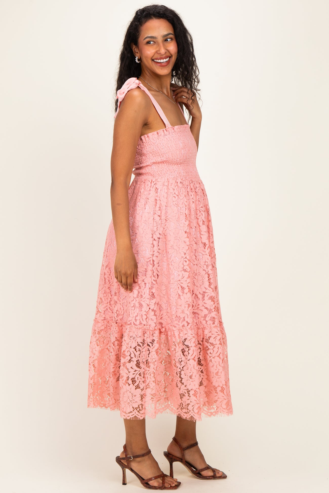 woman wearing a pink lace maternity dress with tie straps and a baby bump visible
