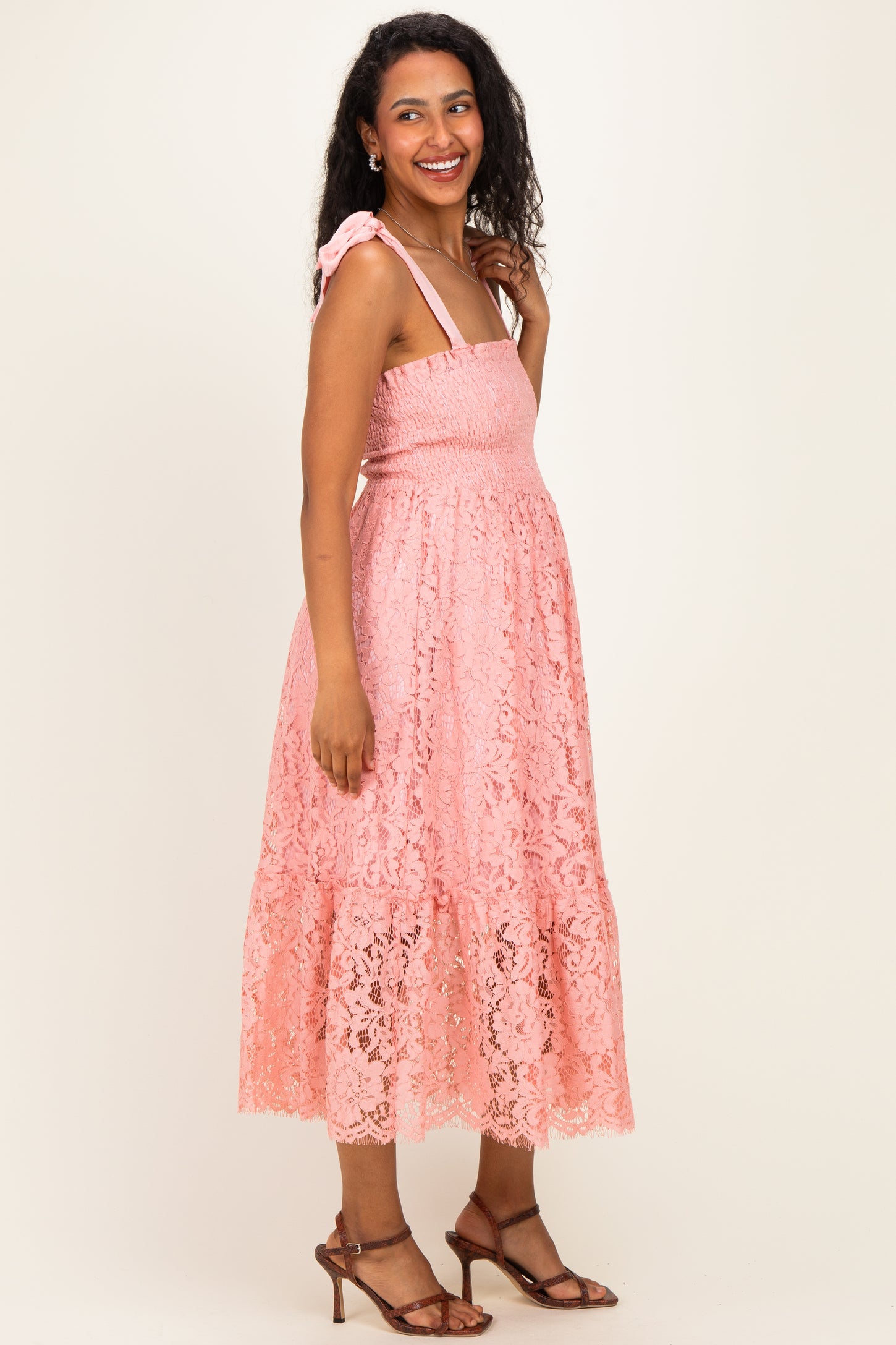 woman wearing a pink lace maternity dress with tie straps and a baby bump visible