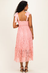 woman wearing a pink lace maternity dress with bow tie straps and a tiered hem, showing a baby bump from the back
