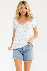 woman wearing a white short sleeve top with blue floral print and light denim cut-off shorts