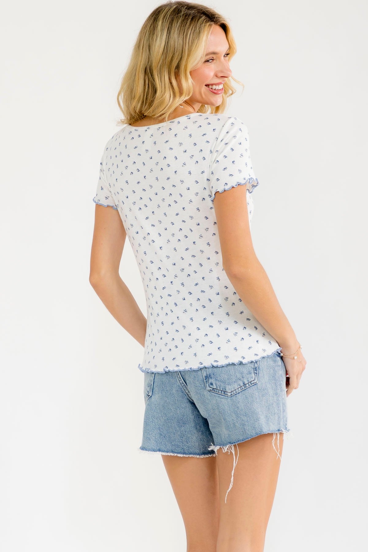 woman wearing a white short sleeve top with blue floral print and ruffled detail, paired with denim shorts