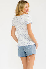 woman wearing a white short sleeve top with blue floral print and ruffled detail, paired with denim shorts