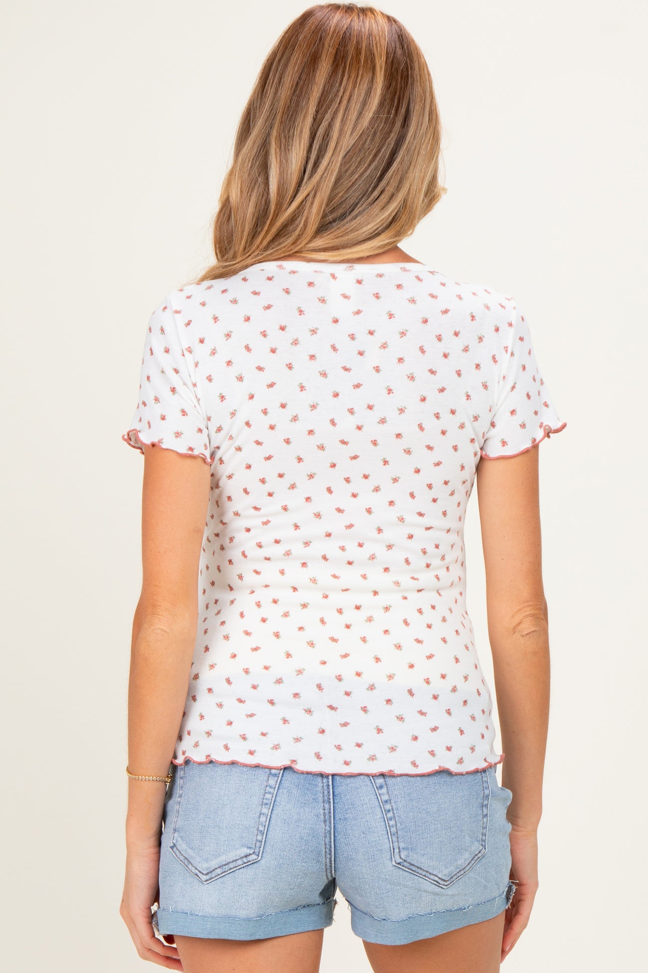 woman wearing a white maternity top with a floral pattern and ruffled short sleeves, paired with denim shorts
