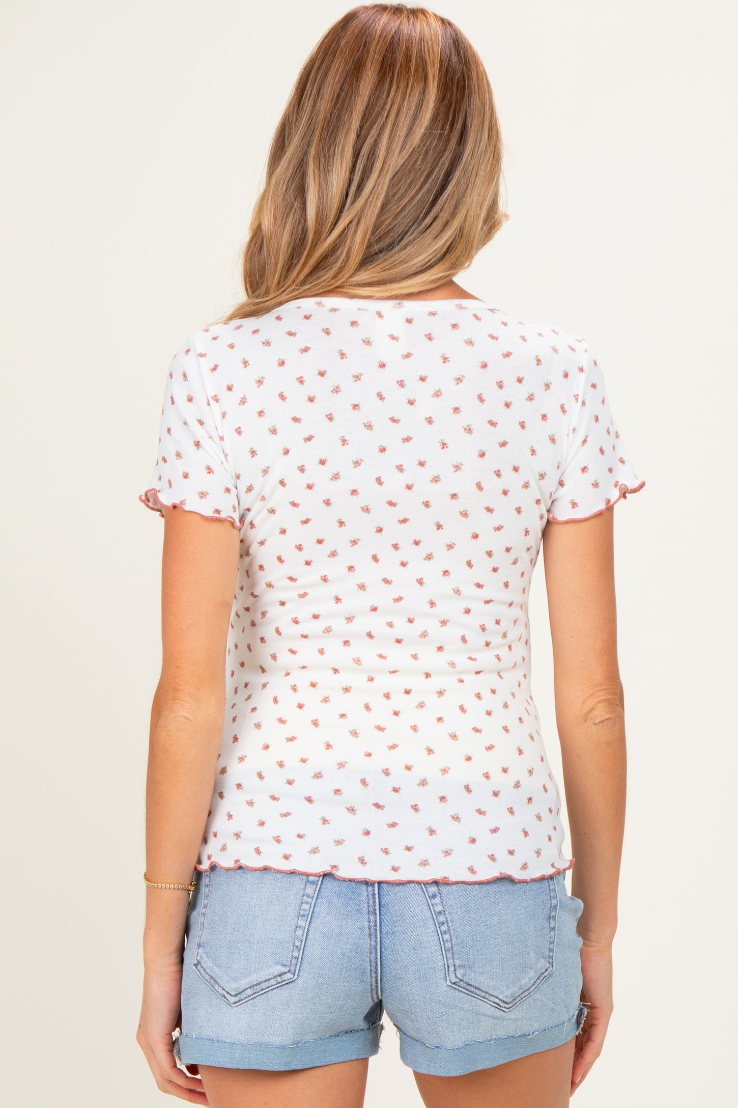 woman wearing a white maternity top with a floral pattern and ruffled short sleeves, paired with denim shorts