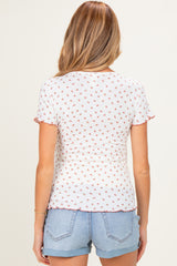 woman wearing a white maternity top with a floral pattern and ruffled short sleeves, paired with denim shorts