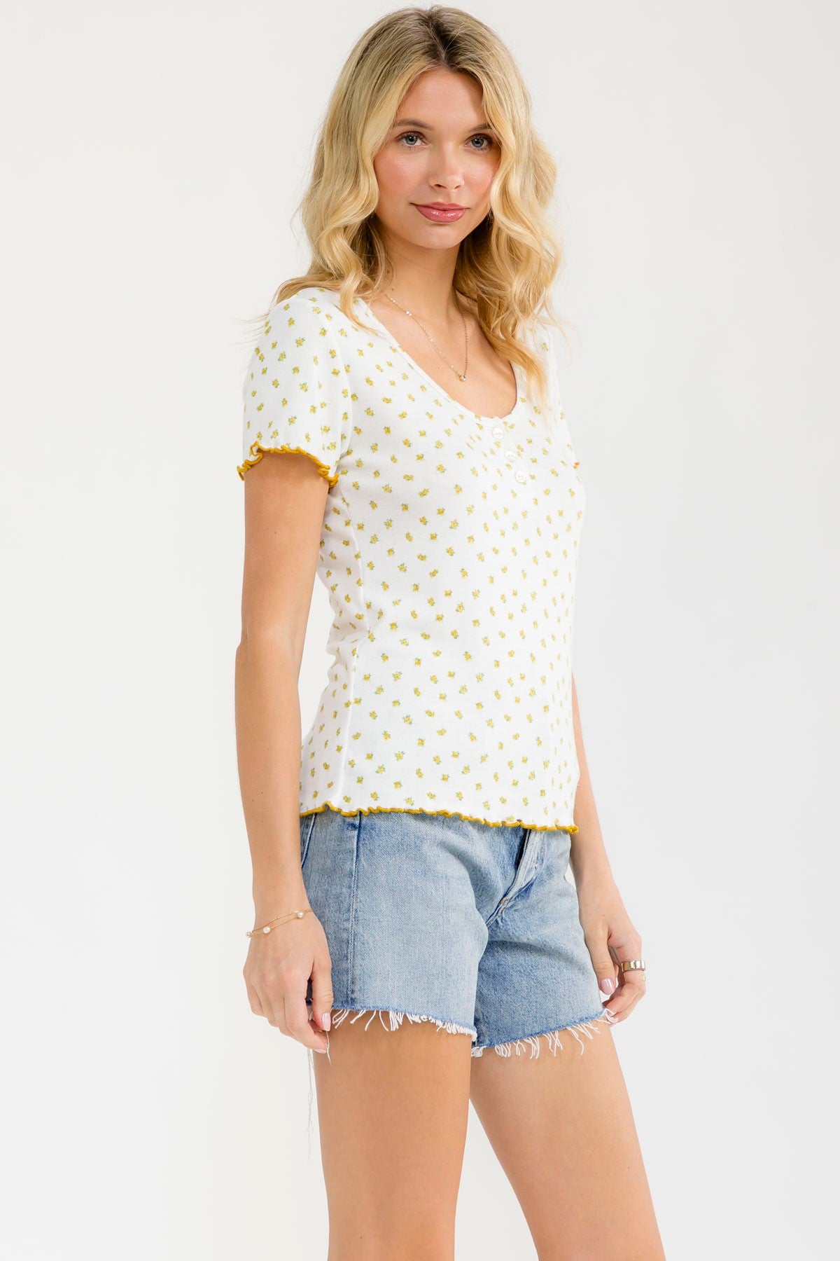 woman wearing a white short sleeve top with yellow floral print and v-neckline paired with denim shorts