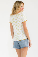 woman wearing a white short sleeve top with yellow floral print and scalloped edges, paired with denim shorts