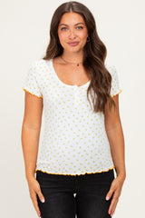 woman wearing a white maternity top with yellow flower prints and scalloped edges, showing her baby bump