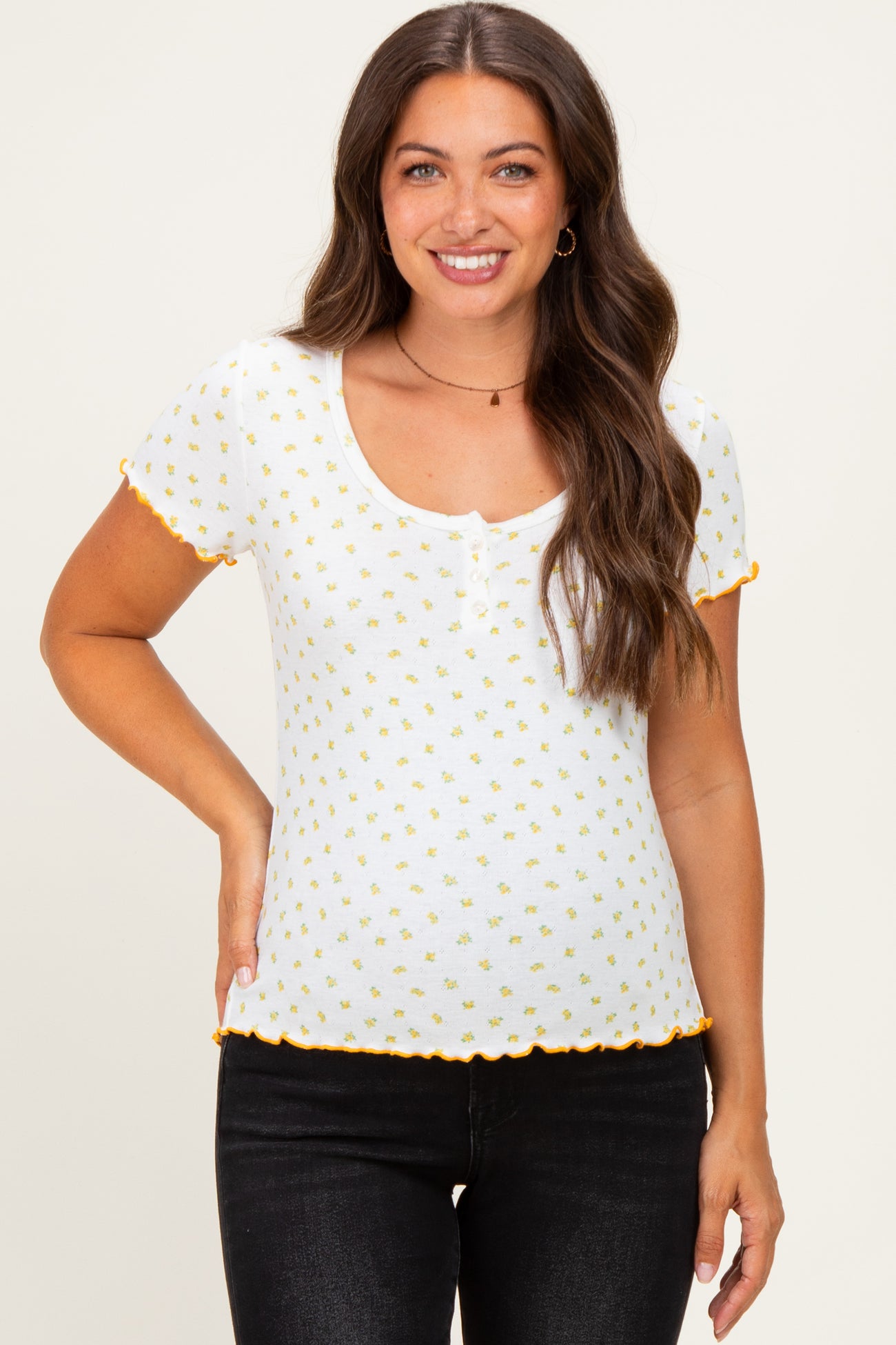 woman wearing a white maternity top with yellow floral print and scalloped orange trim, smiling at the camera