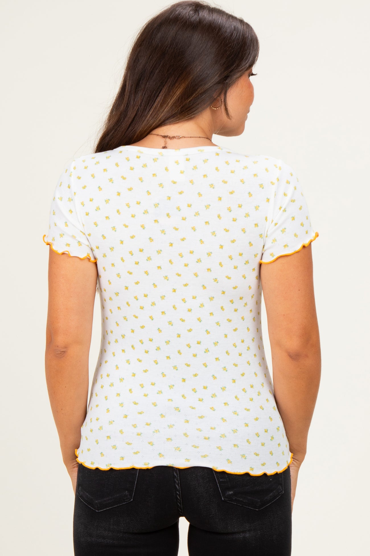 woman wearing a white maternity top with yellow floral print and orange scalloped sleeves, showing her back