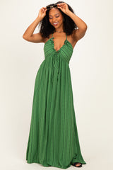 woman wearing a green halter-style maxi dress with ruffled details and a tie waist, smiling while holding sunglasses