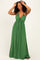 woman wearing a green halter-style maxi dress with ruffled details and a tie waist, smiling while holding sunglasses