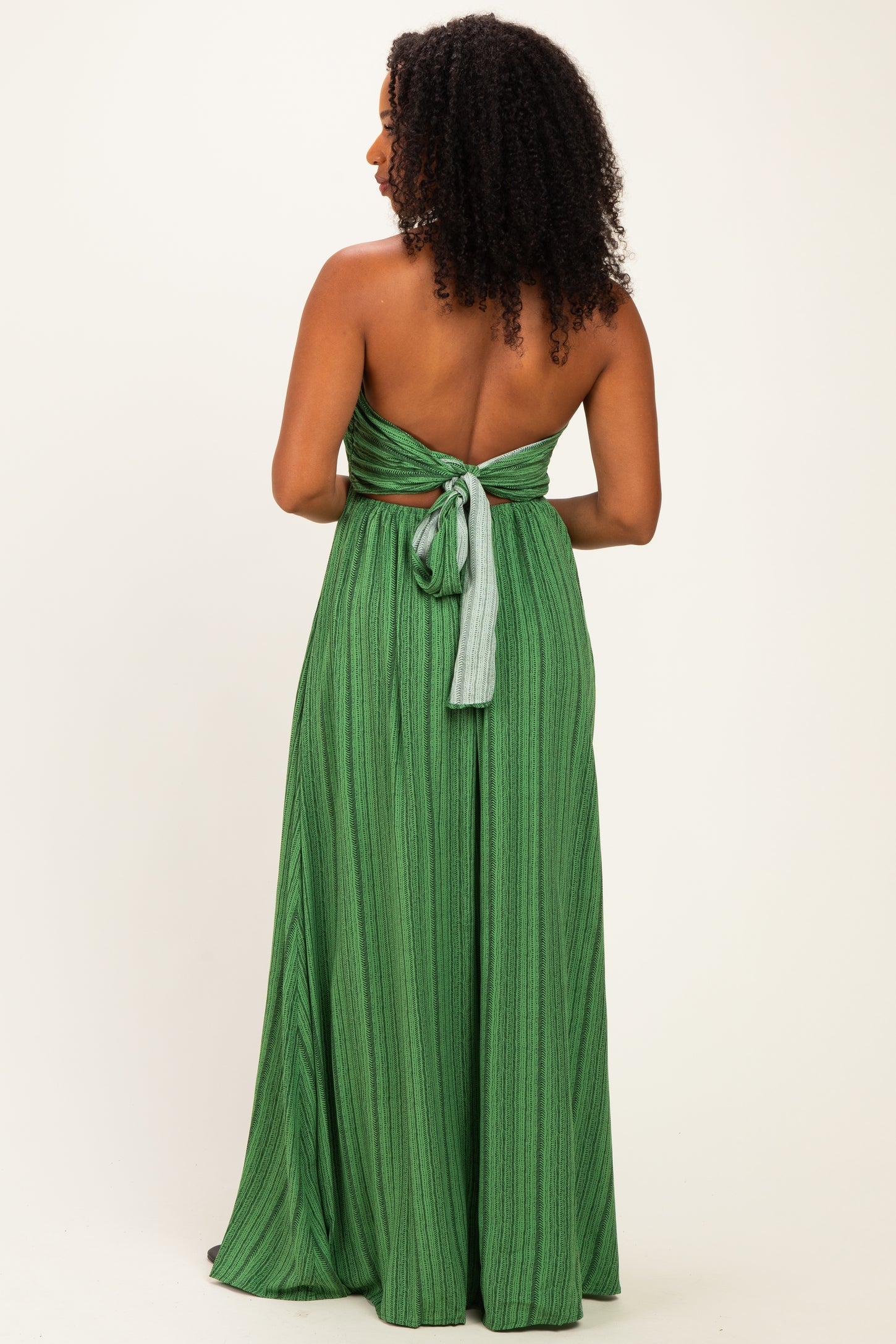 back view of a woman wearing a green striped maxi dress with a tied open back design