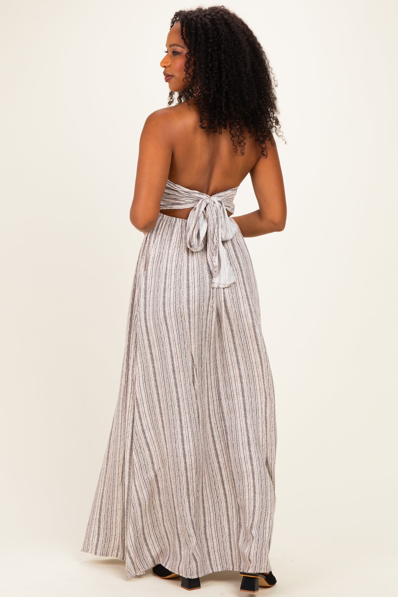 woman wearing a backless striped maxi dress with a tied bow detail at the waist