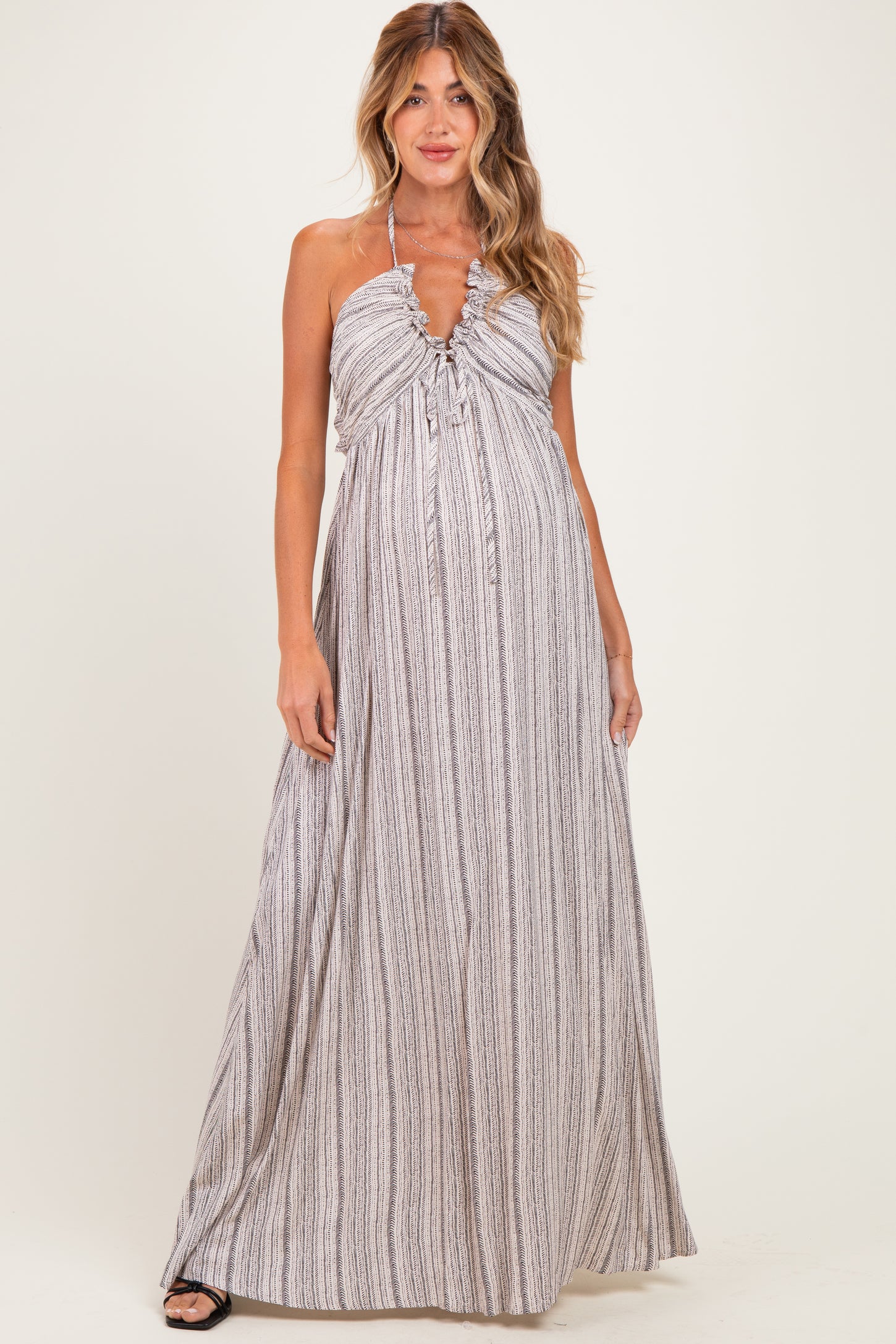 woman wearing a striped maternity maxi dress with a halter neckline and ruffled detailing, showcasing a baby bump