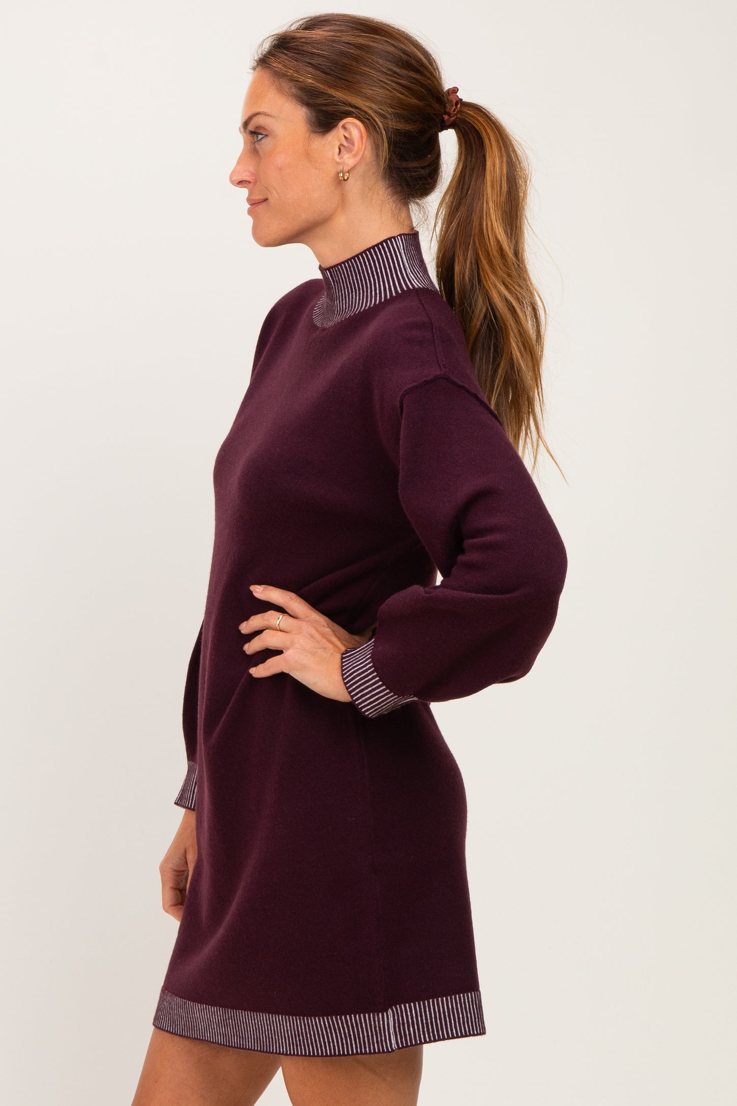 woman wearing a burgundy long sleeve sweater dress with a mock neck and striped cuff details