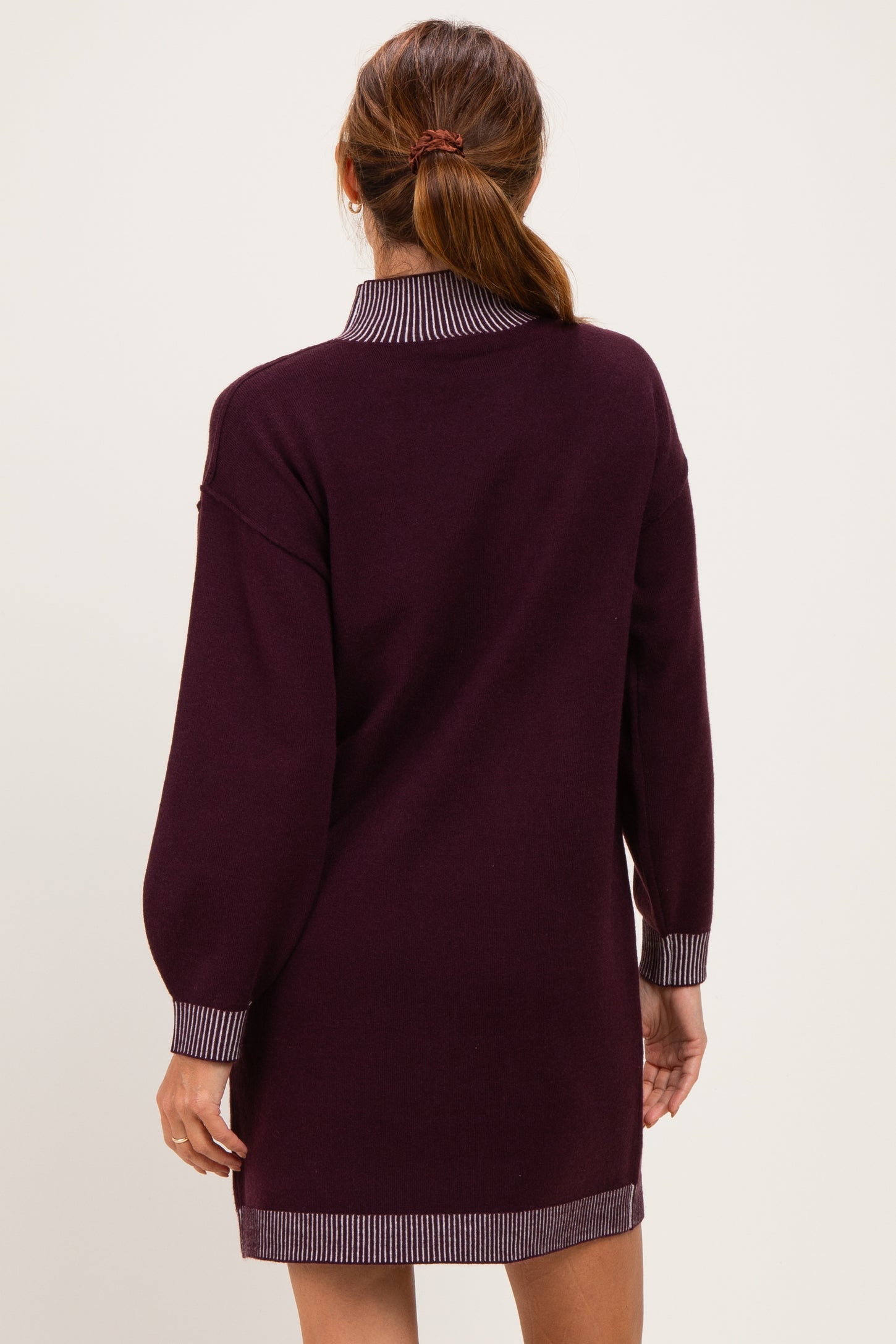 woman wearing a burgundy sweater dress with a striped collar and trim, viewed from the back