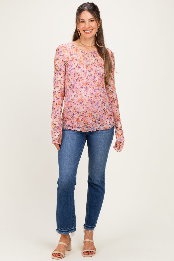 woman wearing a pink floral long sleeve maternity top and blue jeans, highlighting her baby bump