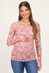 woman wearing a pink floral long sleeve maternity top and holding her baby bump