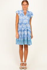 woman wearing a light blue floral print tiered dress with ruffle sleeves and a flared hem, standing against a plain background