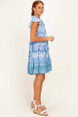 woman wearing a blue floral print dress with ruffle sleeves and a tiered hem, standing sideways