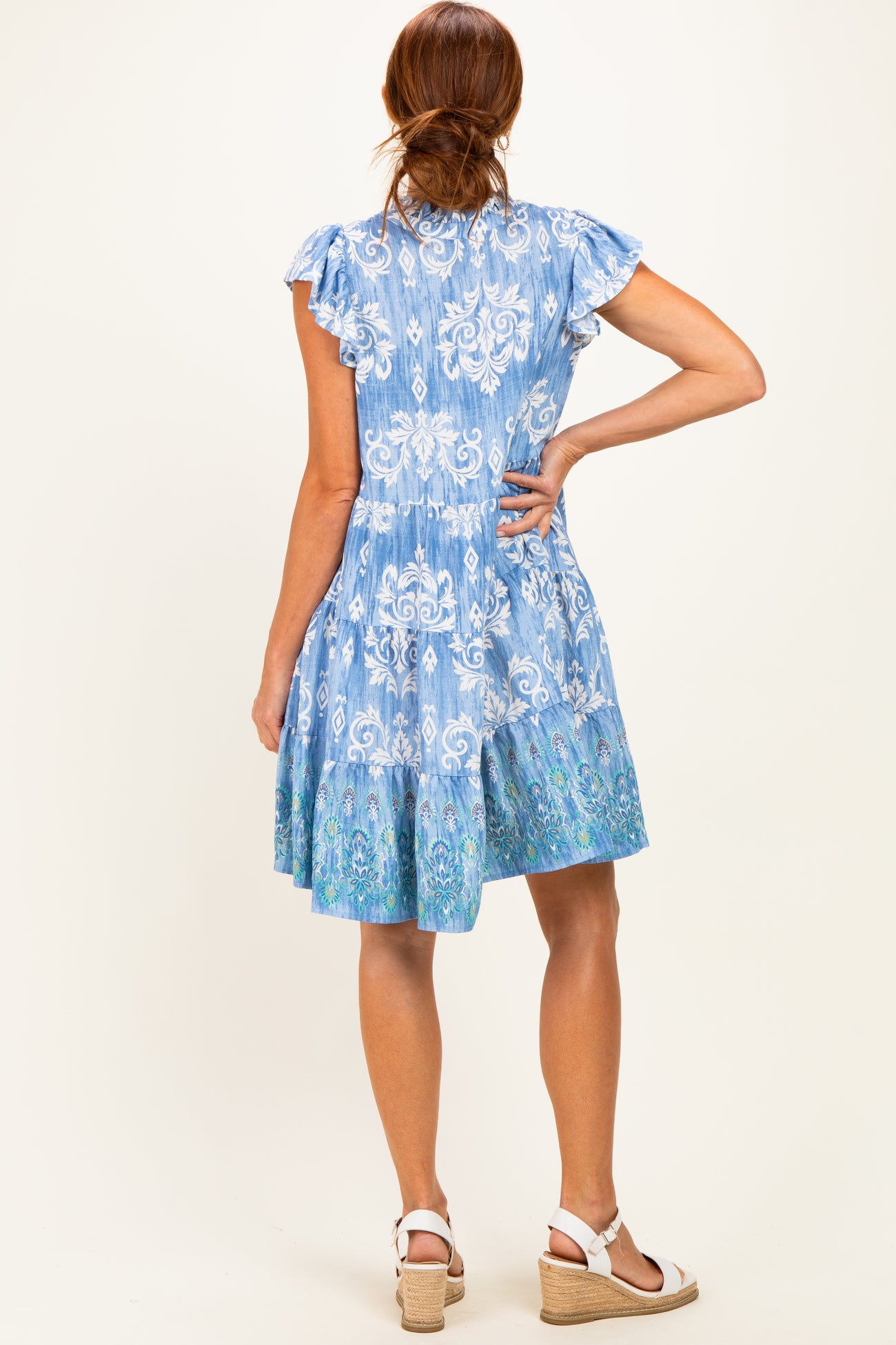 woman wearing a blue floral print short dress with ruffled sleeves and a tiered skirt, viewed from the back