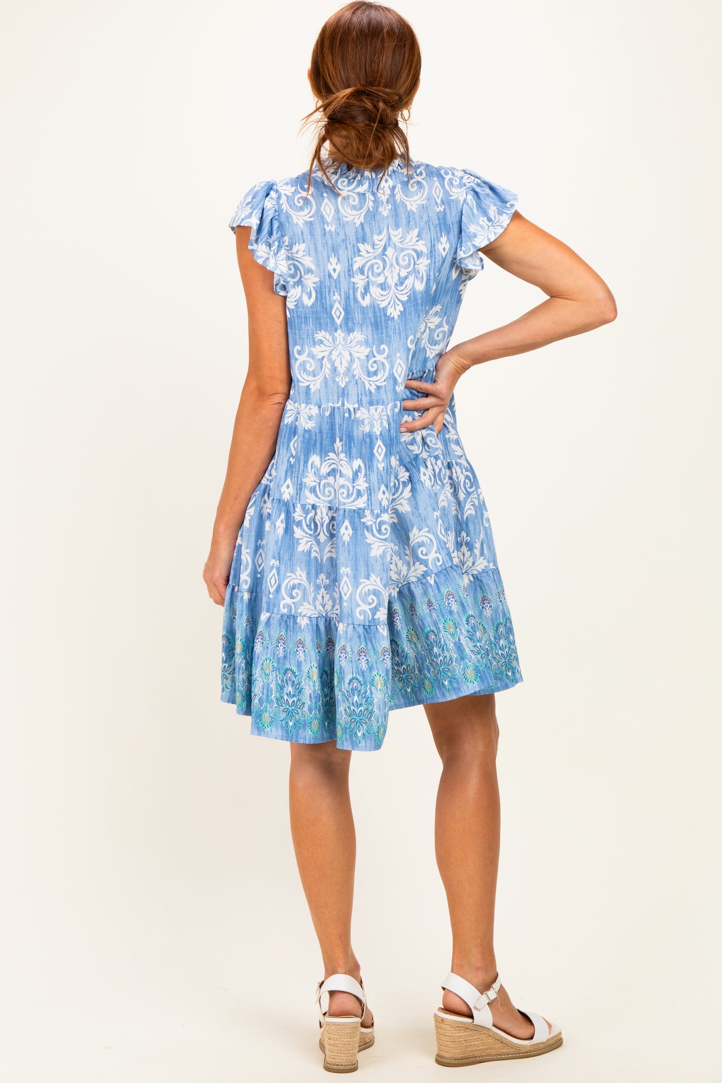 woman wearing a blue floral print short dress with ruffled sleeves and a tiered skirt, viewed from the back