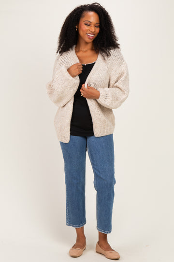 woman wearing a cream chunky knit cardigan over a black tank top and blue straight-leg jeans with beige flats