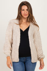 woman wearing a cream oversized maternity cardigan over a black top and blue jeans, showing her baby bump