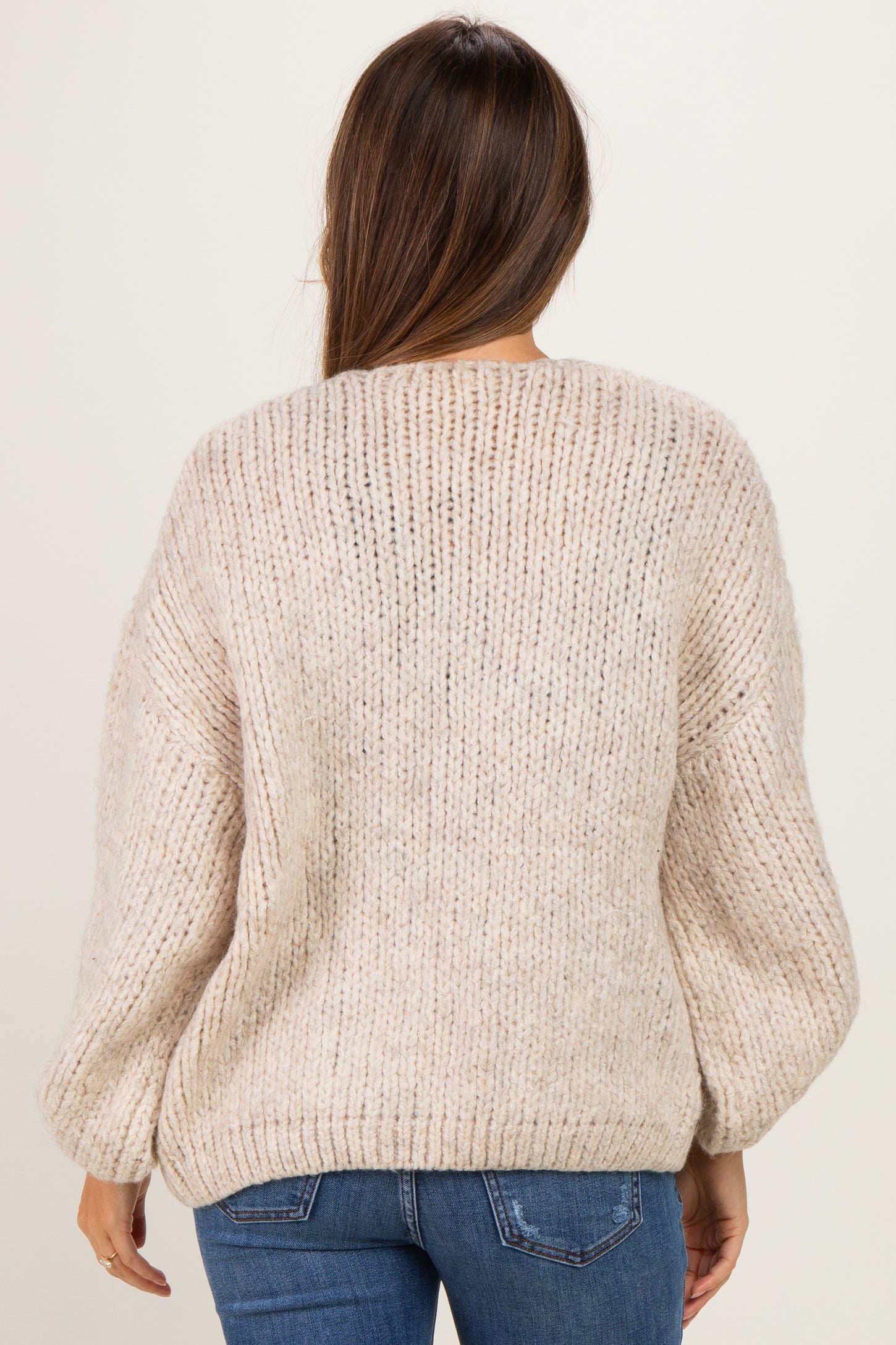 woman wearing a light beige oversized knitted maternity sweater, shown from the back with textured detail
