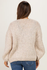 woman wearing a light beige oversized knitted maternity sweater, shown from the back with textured detail