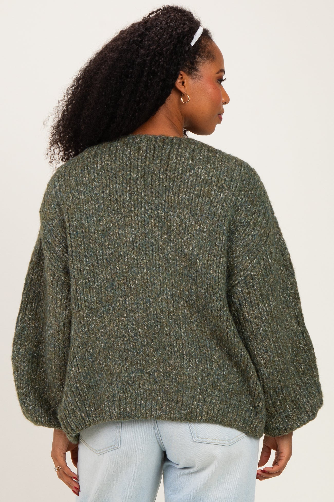 woman wearing a green chunky knit sweater with balloon sleeves, viewed from the back, paired with light denim jeans