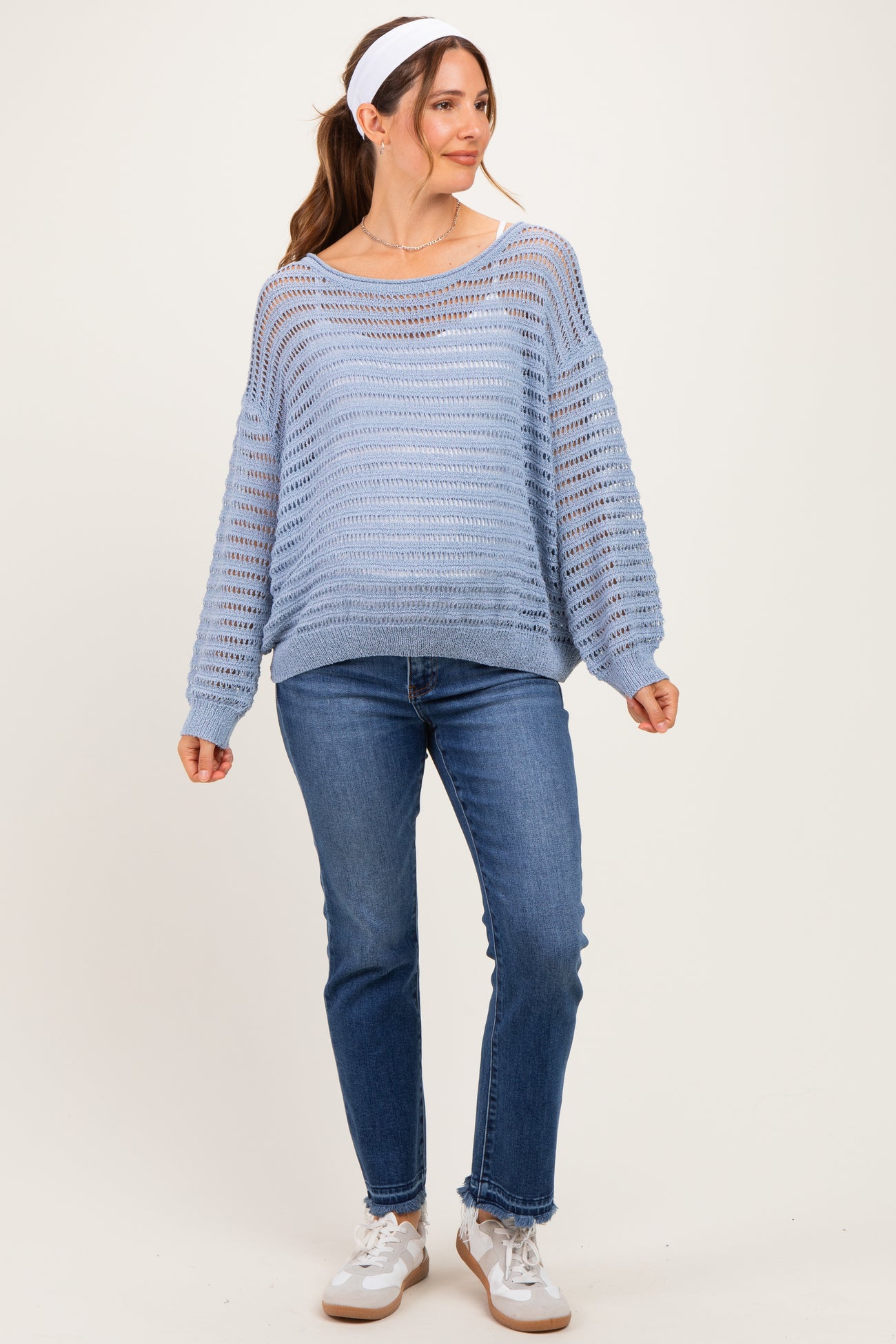 woman wearing a light blue maternity sweater with open knit patterns, paired with blue jeans and white sneakers