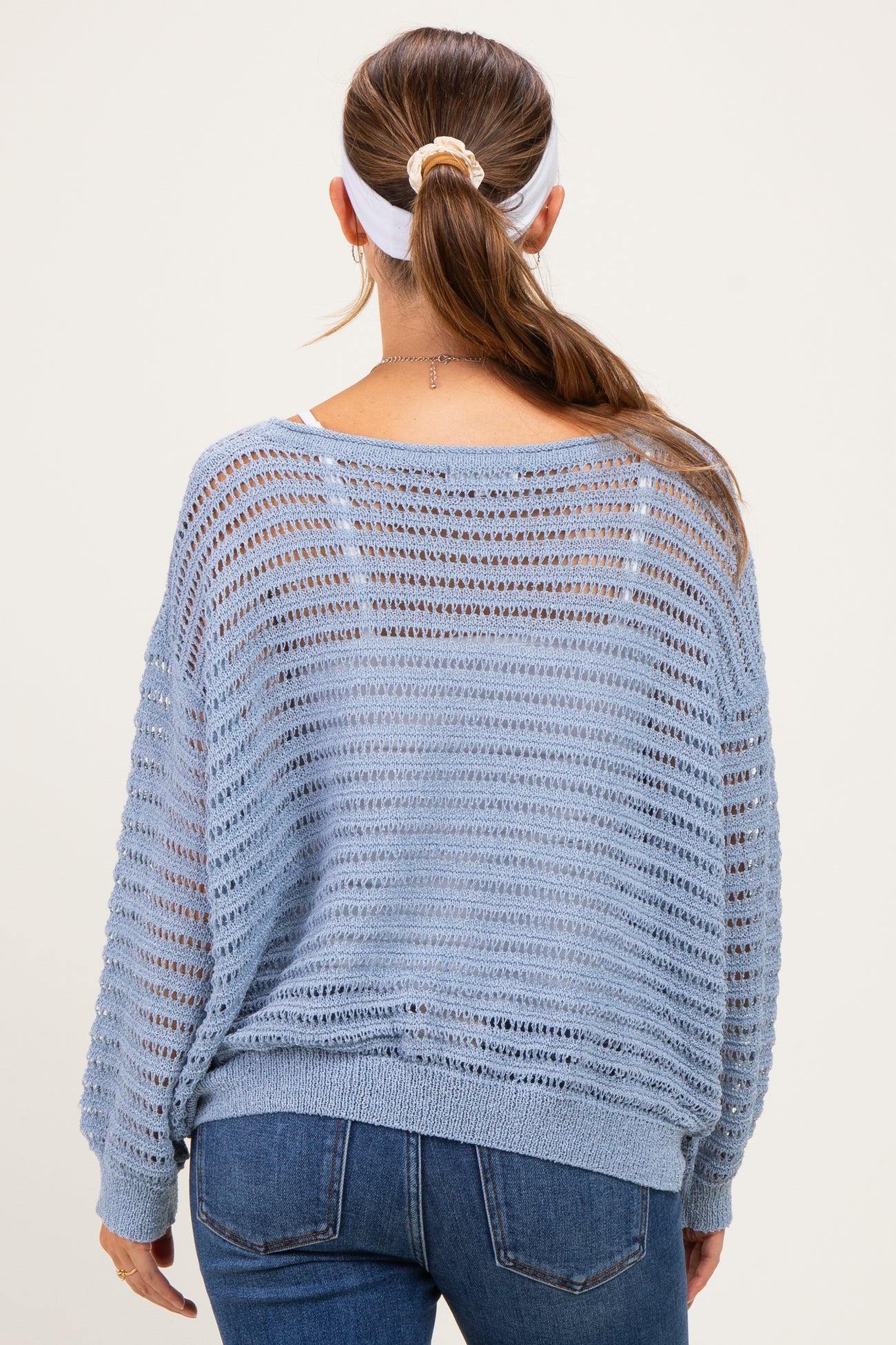 woman wearing a light blue open-knit maternity sweater, viewed from the back, paired with jeans