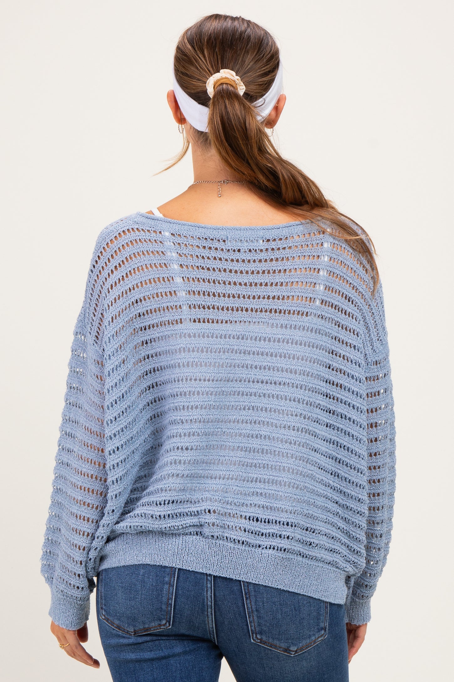 woman wearing a light blue open-knit maternity sweater, viewed from the back, paired with jeans