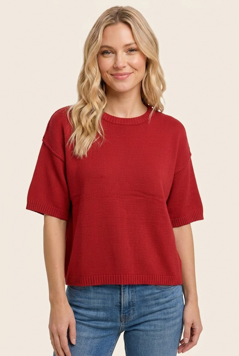 woman wearing a red short sleeve knit sweater with a relaxed fit and round neckline, styled with blue jeans