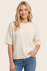 woman wearing a cream short sleeve knit sweater paired with blue jeans