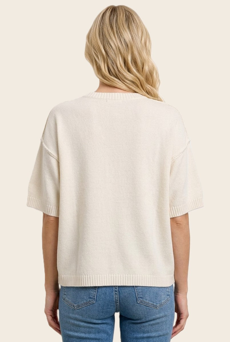 woman wearing a cream oversized sweater with short sleeves, showing the back view, paired with blue jeans